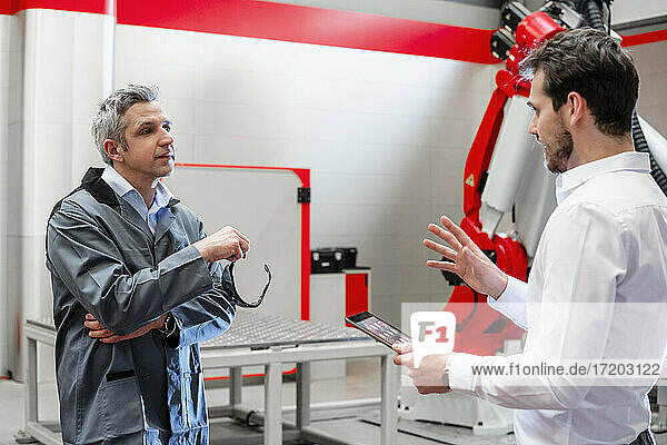 Engineer with digital tablet gesturing while discussing with worker in factory