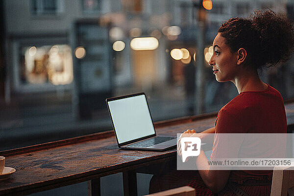 Junge Frau mit Laptop  die wegschaut  während sie an einem Kaffeetisch sitzt