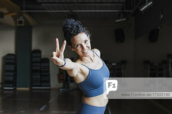 Glückliche weibliche Athletin  die im Fitnessstudio stehend das Friedenszeichen macht