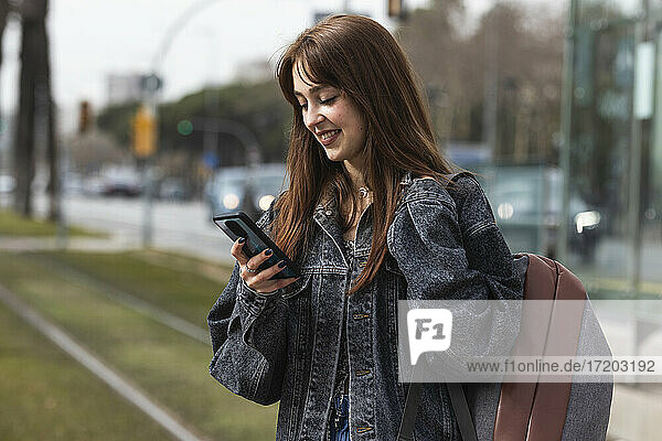 Lächelnde Frau  die ein Smartphone benutzt  während sie an einer Straßenbahnhaltestelle steht