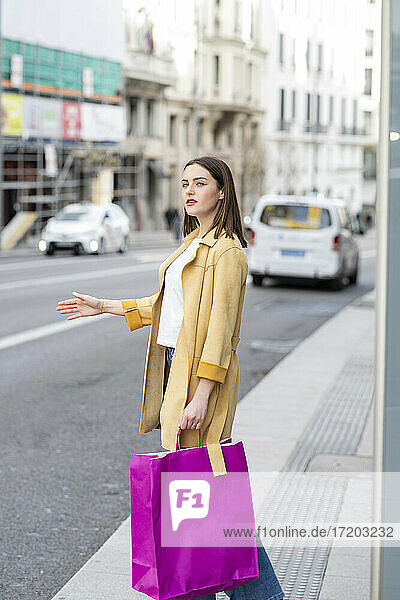 Frau mit Einkaufstaschen  die auf dem Bürgersteig stehend ein Taxi ruft