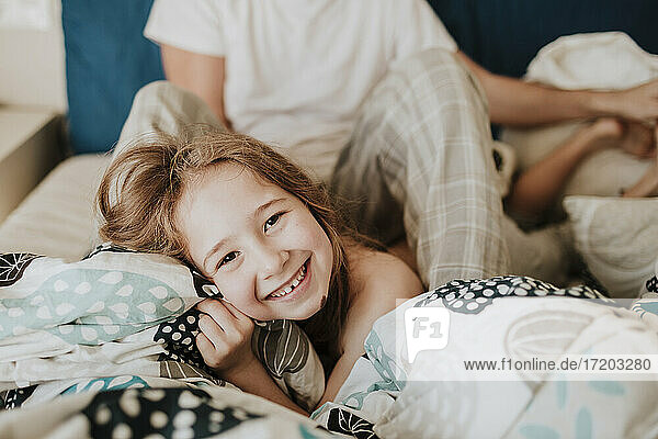Fröhliches Mädchen auf dem Bett liegend mit Vater im Hintergrund sitzend