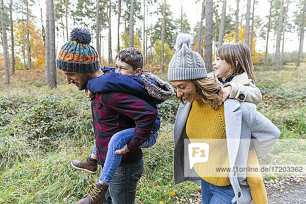 Lächelnde Eltern  die ihre Kinder beim Spaziergang im Wald huckepack nehmen