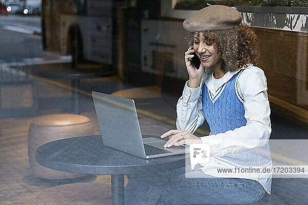 Teenager-Mädchen mit Laptop  das in einem Café mit einem Mobiltelefon spricht