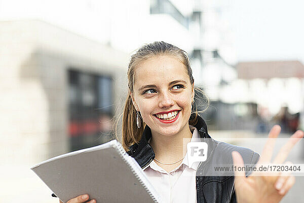 Porträt einer jungen blonden Frau  die mit einem Notizblock in der Hand im Freien steht