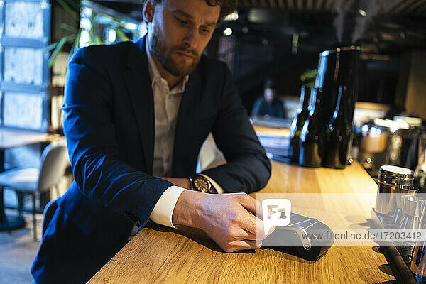 Businessman doing contactless payment through credit card reader at cafe