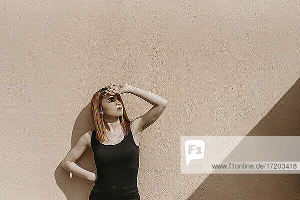 Beautiful redhead woman standing against wall while looking away