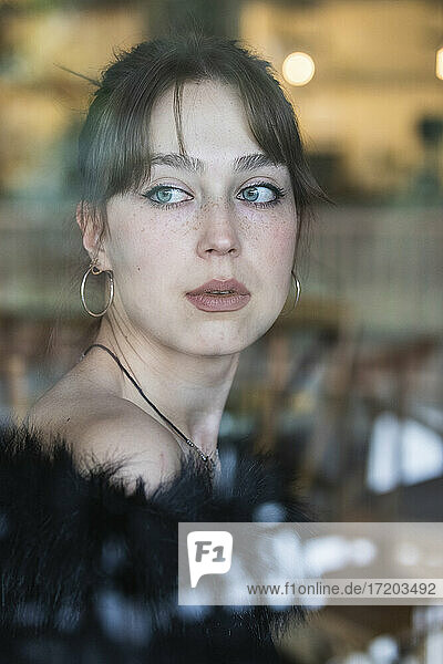 Schöne Frau mit blauen Augen schaut durch ein Fenster in ein Café