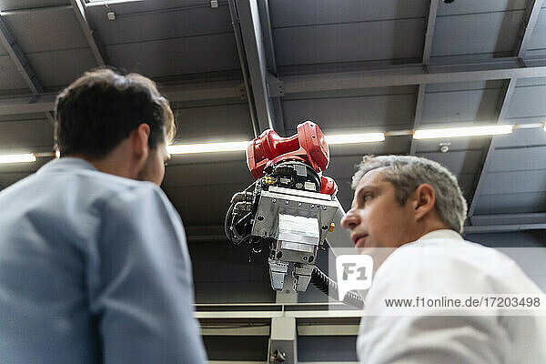 Male engineers discussing at robotic arm in factory