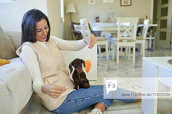 Playful woman showing toy to dog while sitting at home