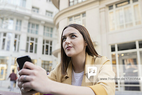 Beautiful woman with smart phone looking away in city