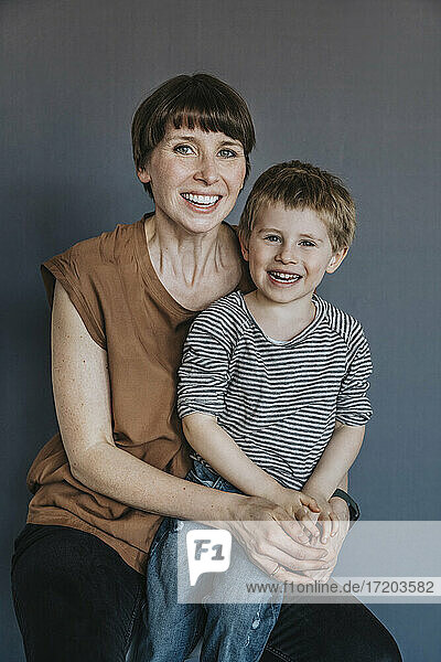 Mutter und Sohn sitzen vor grauem Hintergrund