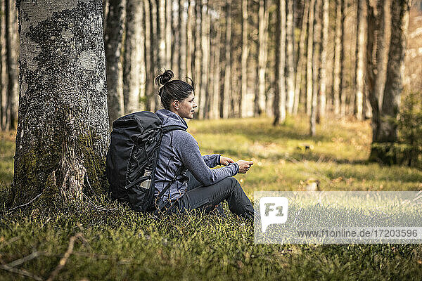 Rucksacktourist  der unter einem Baum im Wald sitzt und sich ausruht