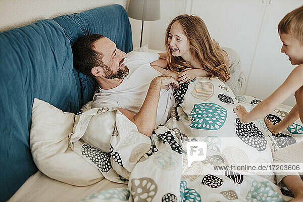 Lächelnde Tochter und Sohn haben Spaß mit Vater auf dem Bett zu Hause