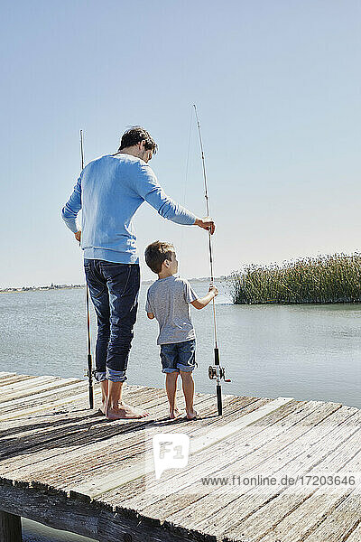 Father and son holding fishing rod while standing on pier