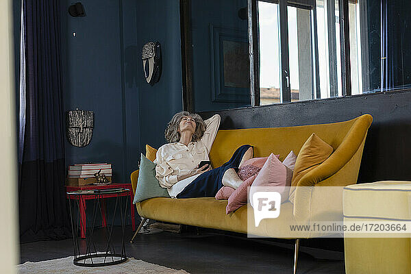 Ältere Frau mit digitalem Tablet entspannt sich auf dem Sofa zu Hause