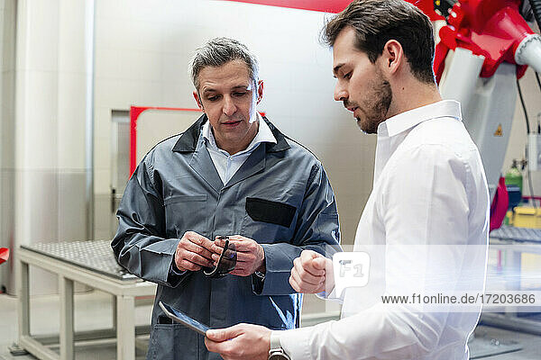 Männlicher Ingenieur  der ein digitales Tablet benutzt  während er mit einem Arbeiter in einer Fabrik diskutiert