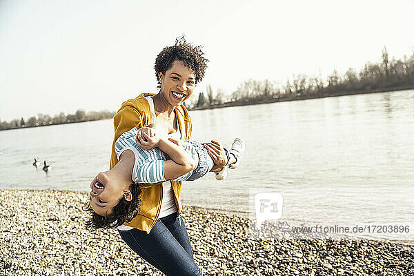 Happy woman carrying son while playing by lake on sunny day