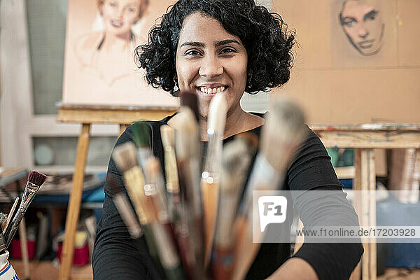 Lächelnde junge Malerin mit Pinseln im Kunstatelier