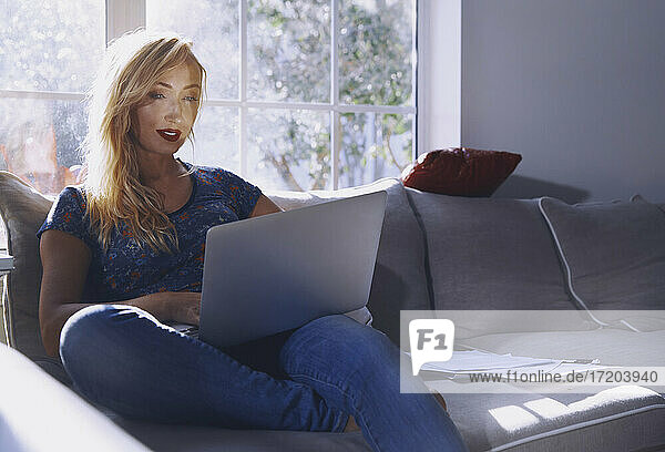 Frau benutzt Laptop  während sie zu Hause auf dem Sofa sitzt
