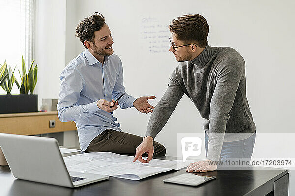 Male entrepreneur discussing with colleague over blueprint at office
