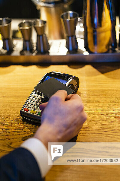 Mann hält Kreditkarte in der Nähe des Lesegeräts für die Zahlung in einem Cafe