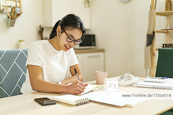 Smiling woman writing in book at home