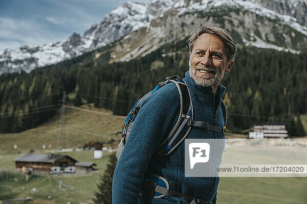 Lächelnder reifer Mann mit Rucksack  der wegschaut  während er am Hochkonig steht  Salzburger Land  Österreich