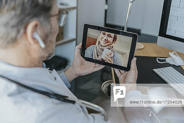 Männlicher Angestellter im Gesundheitswesen im Gespräch mit einem Patienten über ein digitales Tablet  während er in der Arztpraxis sitzt