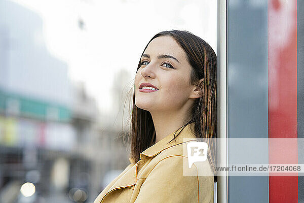 Lächelnde Frau mit braunem Haar  die sich an die Wand lehnt und wegschaut