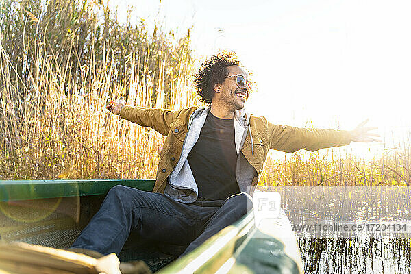 Unbekümmerter Mann mit ausgestreckten Armen  der lächelnd in einem Kanu auf einem Fluss sitzt