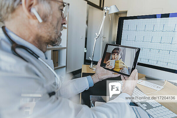 Allgemeinmediziner im Gespräch mit einem Patienten per Videoanruf über ein digitales Tablet in der Arztpraxis