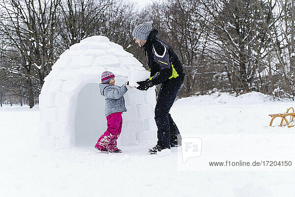 Girl with help of father carrying snow block to build igloo at park