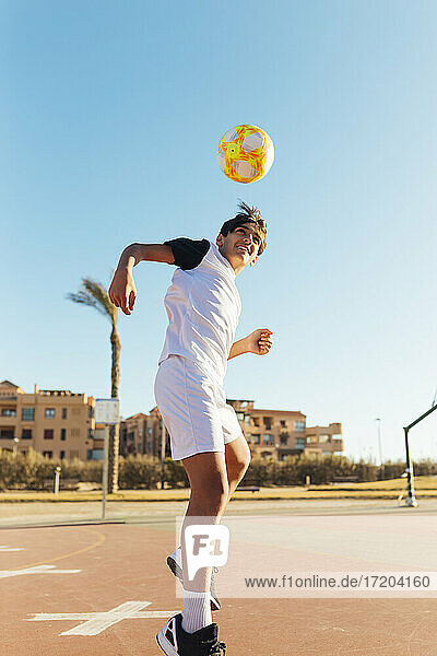 Junge köpft Fußball auf Sportplatz gegen Himmel