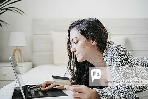Woman with credit card doing online shopping while using laptop on bed