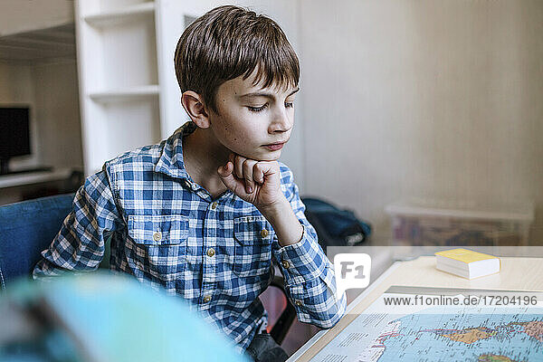 Junge mit Hand am Kinn studiert Karte am Tisch