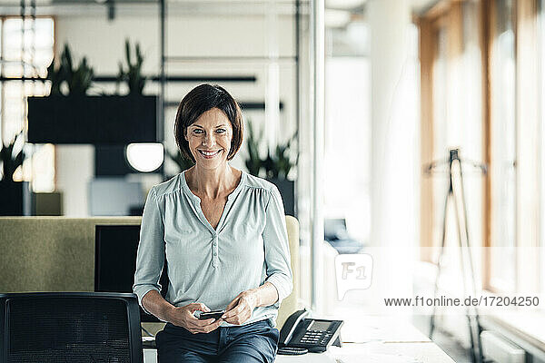 Happy businesswoman with smart phone in office