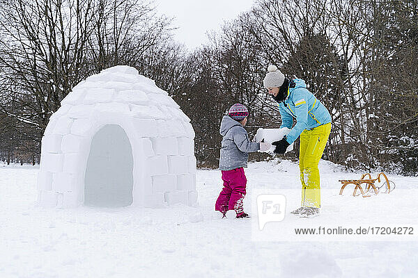 Mother helping daughter to carry snow block at park
