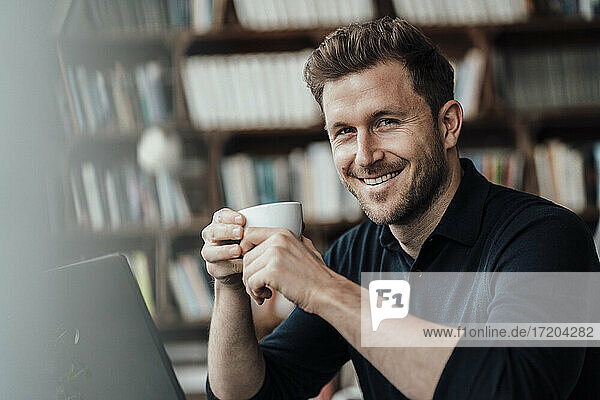 Smiling businessman having coffee while sitting with laptop at cafe