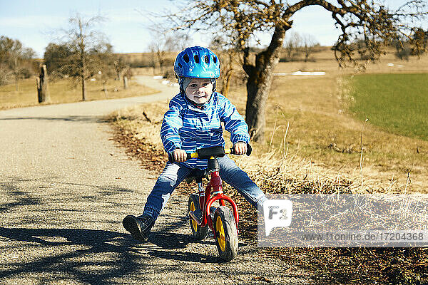 Boy wearing cycling helmet riding balance bike on road during sunny day