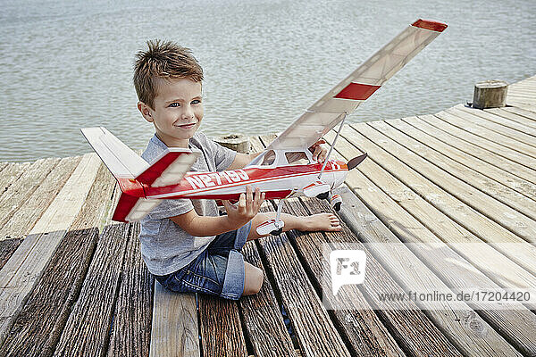 Lächelnd niedlichen Jungen spielen mit Flugzeug Spielzeug auf Pier