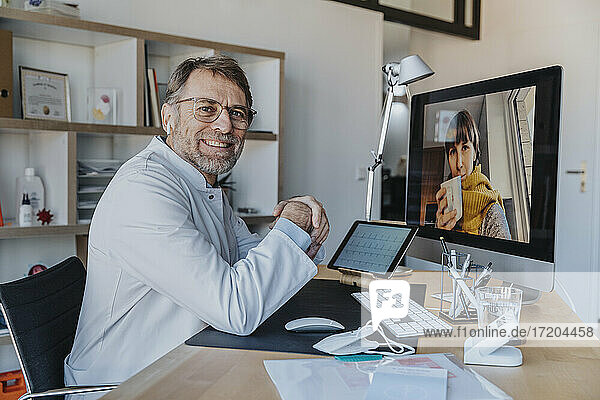 Lächelnder Arzt mit Patientin über Videoanruf am Computer in der Arztpraxis