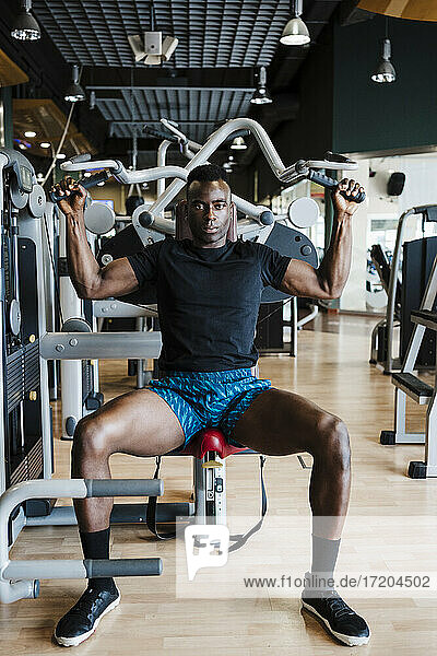 Male athlete sitting on exercising equipment at gym