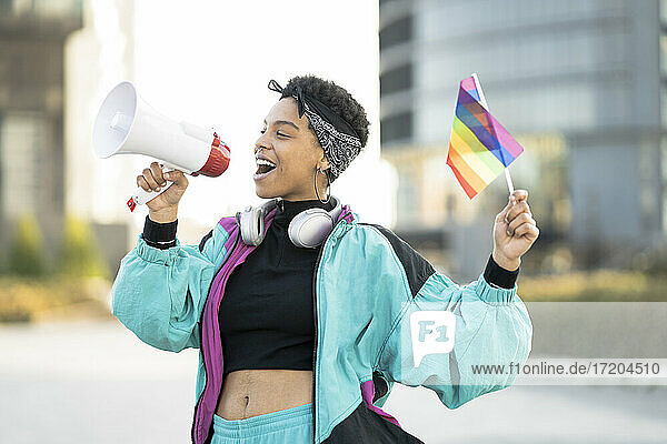 Weibliche LGBTQIA-Demonstrantin hält Regenbogenfahne  während sie durch Megaphon verkündet