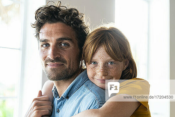 Lächelnde rothaarige Tochter mit blauen Augen kuschelt mit Vater im Wohnzimmer