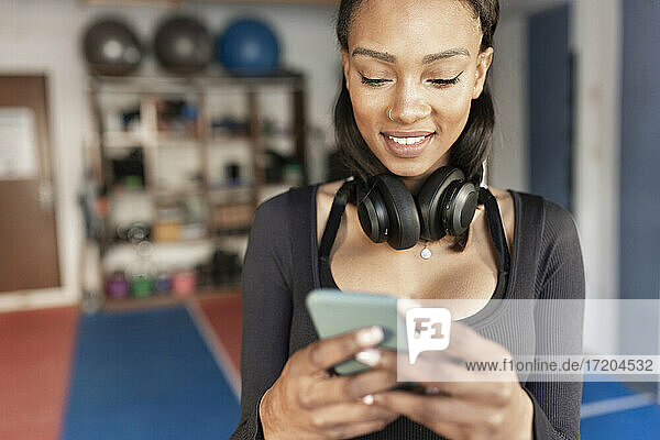 Lächelnde junge Frau  die im Fitnessstudio ein Mobiltelefon benutzt