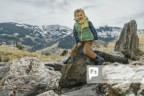 Smiling boy in warm clothing sitting on rock at Salzburger Land  Leogang Mountains  Austria