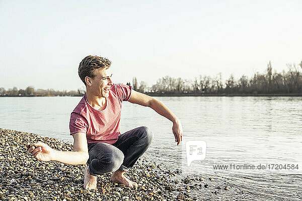 Fröhlicher junger Mann  der an einem sonnigen Tag einen Kieselstein in einen See wirft