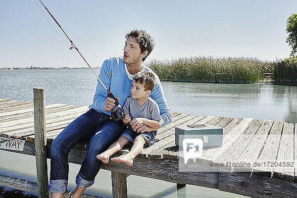 Mature man and boy fishing together while sitting on pier