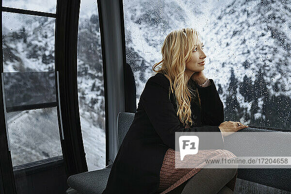 Nachdenkliche blonde Frau  die durch ein Fenster schaut  während sie in einer Seilbahn sitzt